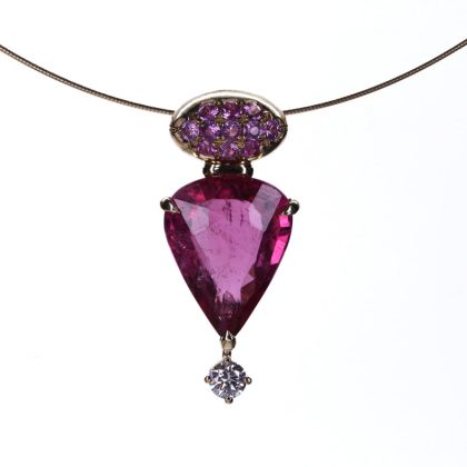 Close-up of an 18K gold pendant with a vibrant 5.29-carat rubellite, pink sapphires, and a sparkling diamond, set on a stainless steel chain.