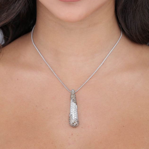 Close-up of a model wearing an 18-karat gold teardrop pendant adorned with sparkling diamonds and brown melee accents, suspended on a delicate chain.